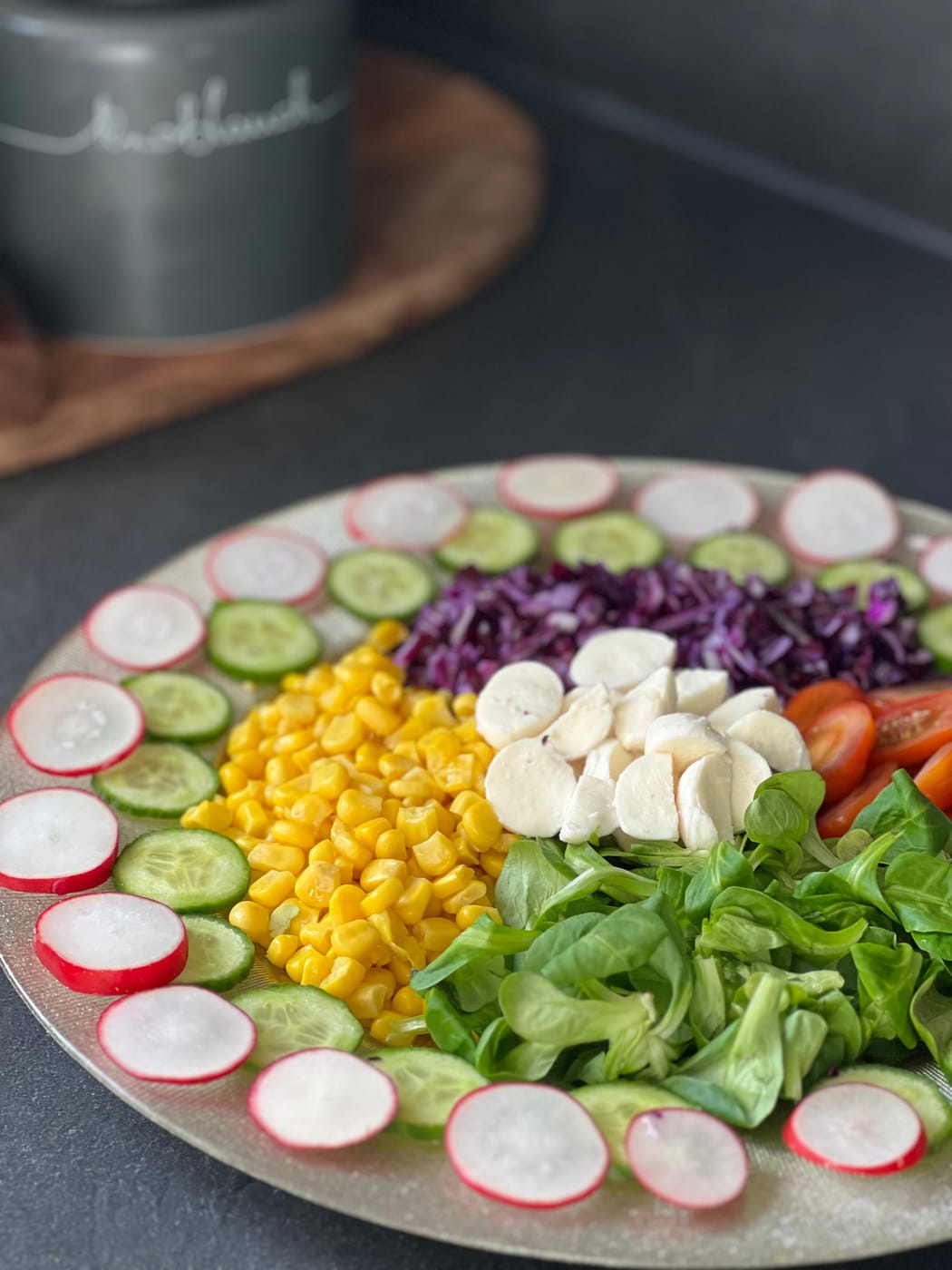 Bunt angerichteter Teller mit Radieschen, Gurken, Mais, Mozzarella, Tomaten und Feldsalat