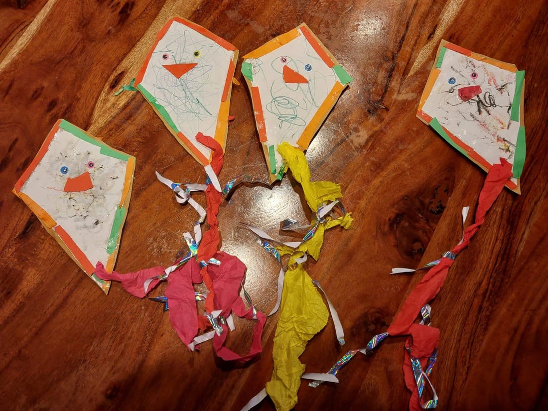 Vier bunte gebastelte Papierdrachen mit Kreppband-Schwänzen liegen auf dem Tisch