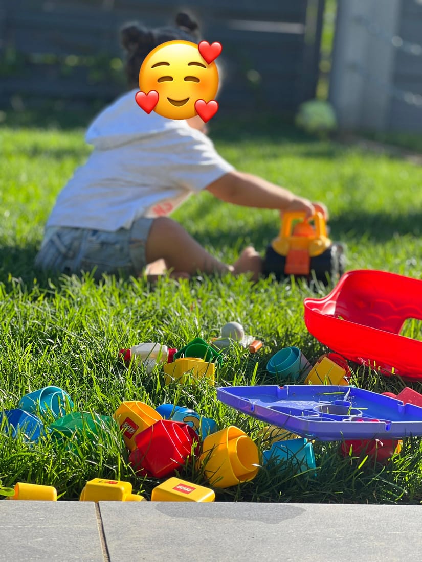 Ein Kind spielt auf dem Rasen mit großen bunten Bausteinen und einer roten Rutsche