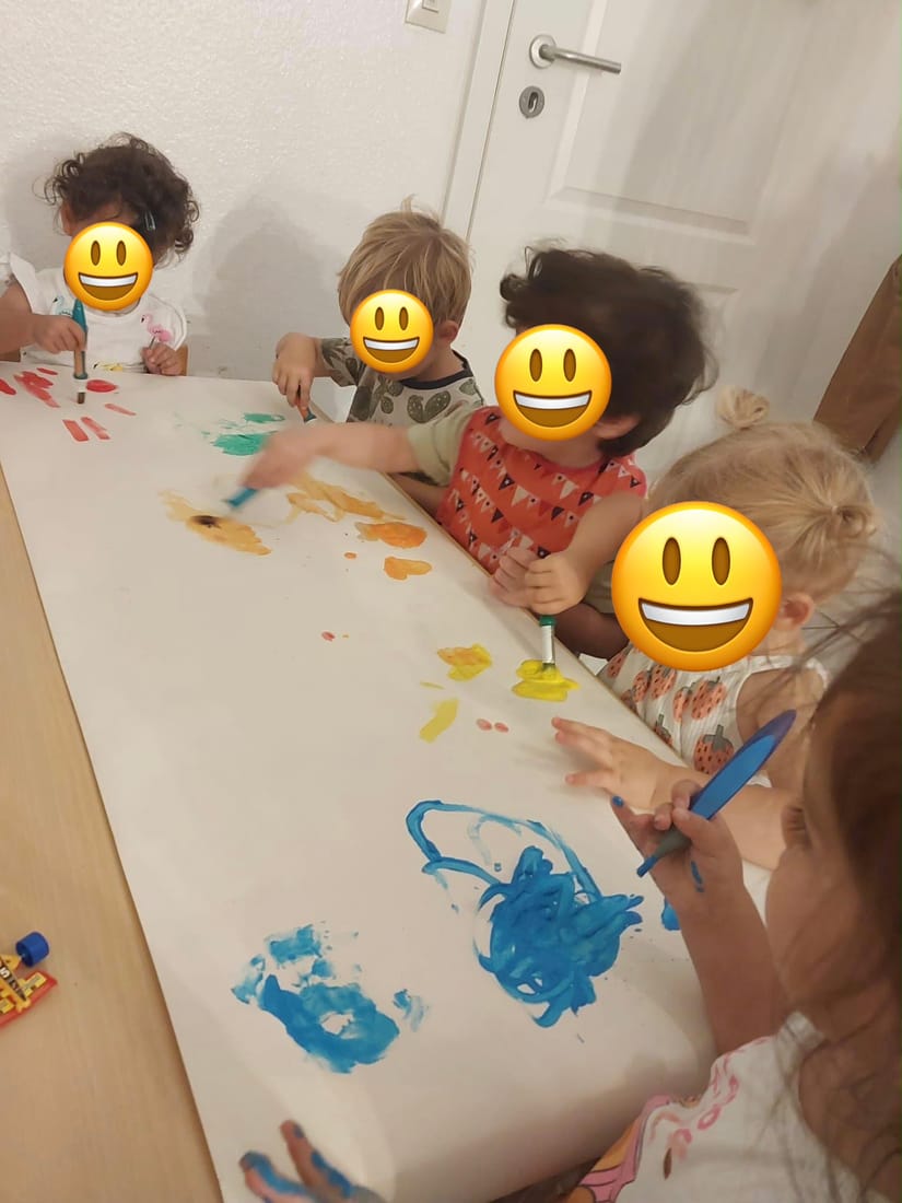 Fünf Kinder malen zusammen mit Pinseln und bunten Farben an einem großen Blatt Papier