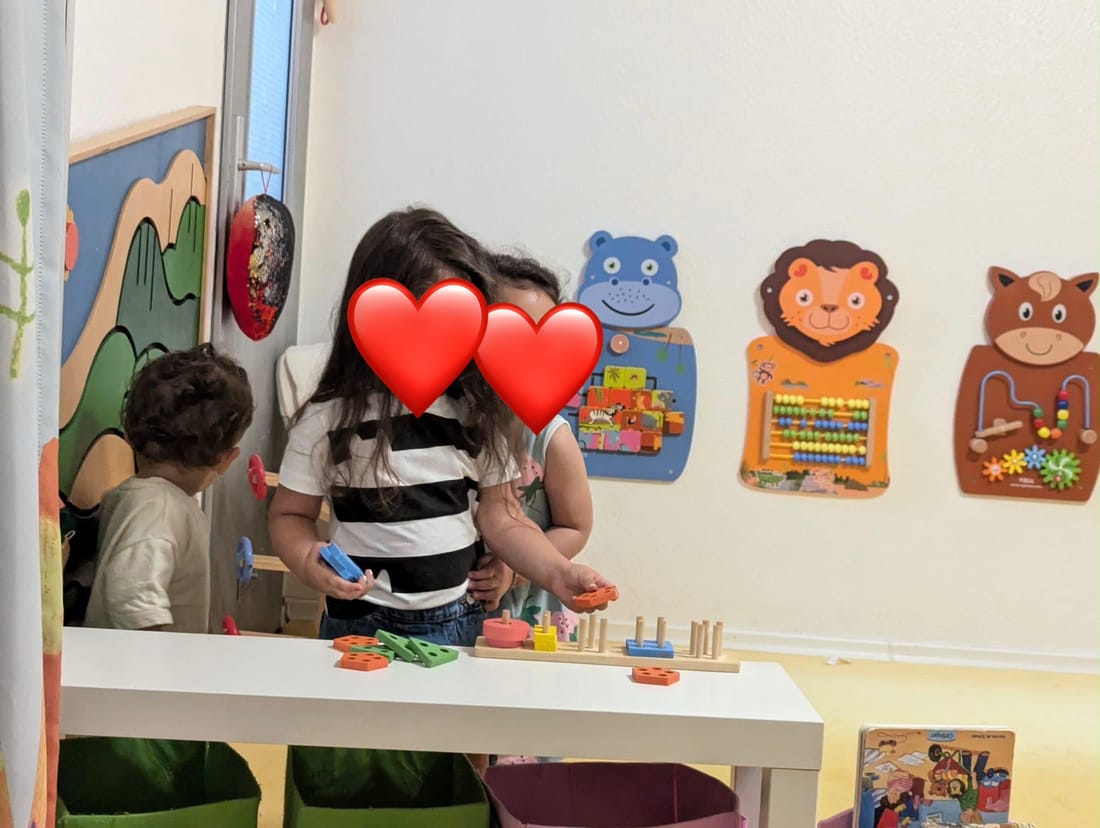 Kinder spielen im Spielzimmer an einem Tisch mit bunten Steckspielen, an der Wand hängen Motorik-Tafeln
