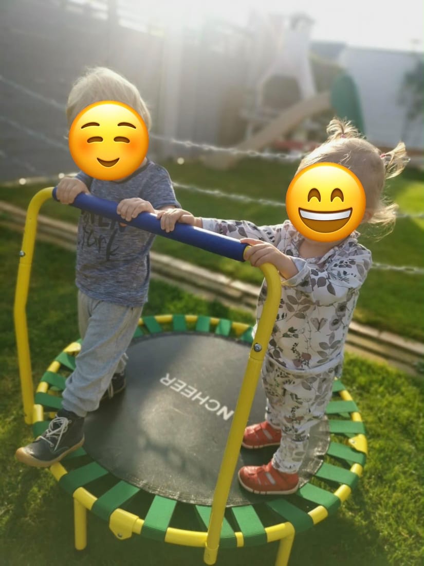 Zwei Kinder stehen lachend auf dem kleinen Gartentrampolin mit Haltegriff