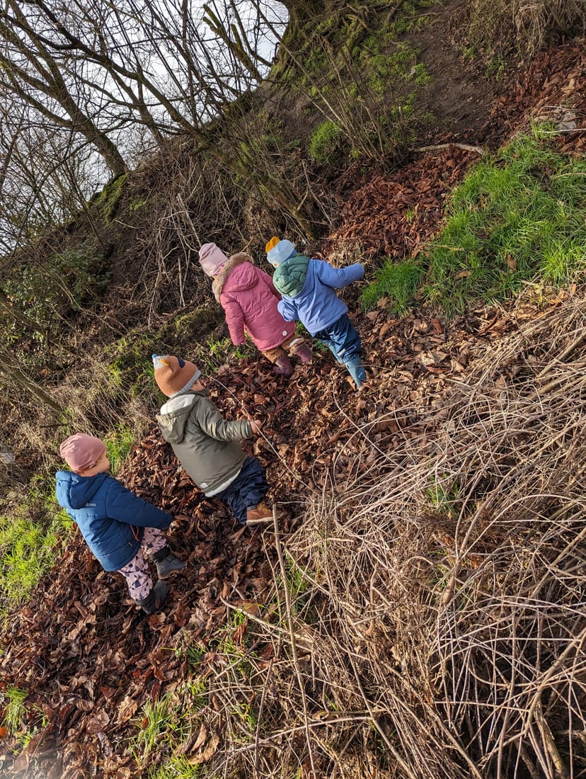 Vier warm eingepackte Kinder erkunden im Winter einen Waldhang